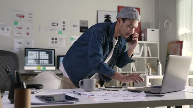 Asian man Graphic designer talking on mobile phone while working in office. Artist Creative Designer Illustrator Graphic Skill Concept.