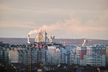 Cement plant with high factory structure and tower cranes at industrial production area near city urban area. Manufacture and global industry concept