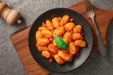 A plate of POTATO GNOCCHI with tomato sauce on a wooden cutting board. Top view.