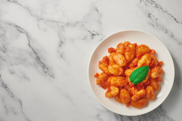 A plate of freshly prepared POTATO GNOCCHI in tomato sauce on a marble background. Top view. Copy space.