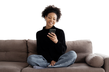 The curly-haired woman smiles uses the phone writes sms makes an online order sits on the couch, transparent background.