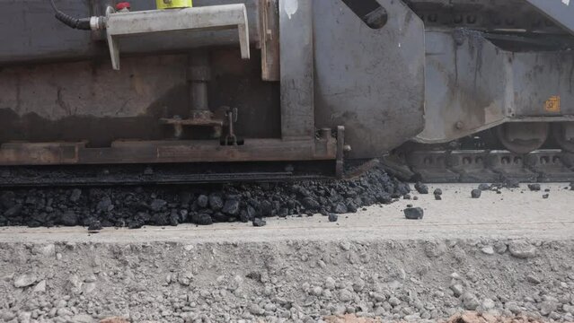 Asphalt distribution by heavy machinery close-up. Asphalt paver lays hot asphalt on road construction site on sunny, clear summer day. Road construction and pavement repair concept.