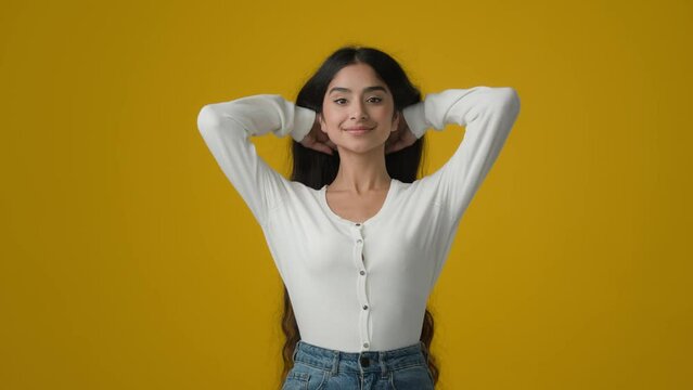 Ethnic Indian girl model with long hair gorgeous beautiful hairstyle in studio yellow background poising. Woman brunette with wavy shiny curls flying in wind hairdo silky hairstyling shampoo recovery