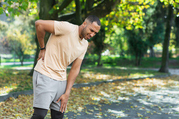 Tired man after jogging in park, hispanic man has severe pain in back and muscles after fitness,...