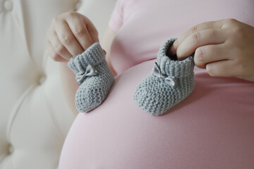 Pregnant woman holding two little wool booties on belly. Healthy pregnancy.