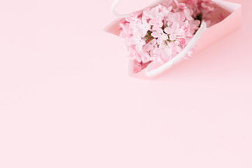 Spring pink flowers. Gift bag and lilac branches on pink background. Flat lay, top view, copy space