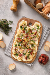 Homemade butterboard with onion, garlic, sun-dried tomatoes, herbs, crispy baguette on gray background. View from above. Vertical format. Trendy Butter board.