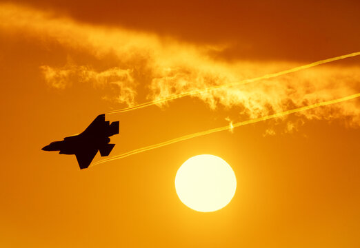 Fighter jet at sunset. Modern military fifth generation fighter jet streaming vapor passing the setting sun. Fighter jet aircraft with orange sky