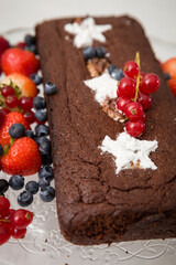 Chocolate brownie cake with fresh blueberries,  raspberries, strawberries, red currant and white stars made of powdered sugar. Homemade cake decorated with fruit. Festive concept