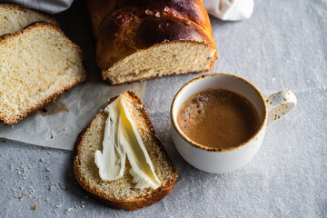 Slice of homemade braided bread with butter and cup of espresso coffee on linen tablecloth 