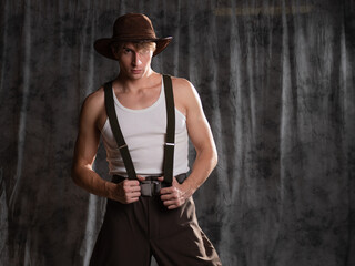 young man in a rural retro style, a character in an adventure western. A guy in a hat and a T-shirt, breeches with suspenders.