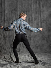 Stylish elegant young man in a blue silk shirt posing in the studio on a gray fabric background