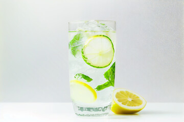 a glass of water with lemon slices, mint leaves, and ice cubes on a light background