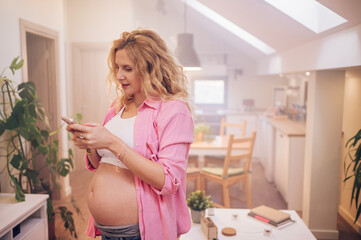 Beautiful pregnant woman using smartphone at home