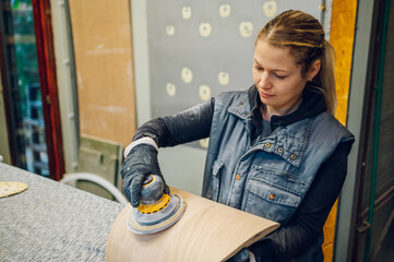 Woman carpenter using an electric sander in a workshop or factory