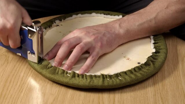 Furniture restoration. A man fixes the paralon on the surface of the chair with a stapler. Upholstery of furniture. Close-up hands