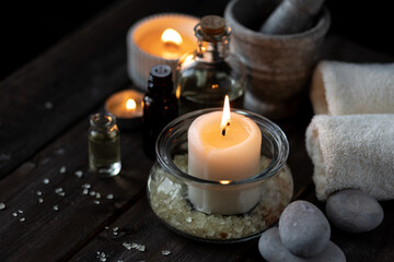 Spa setting with essential oil, candle, sea salt, pebbles, towel on dark wooden background. Massage, aromatherapy. Natural organic ingredients for relaxation, detention. Wellness in salon concept