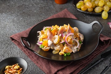 Salad of salted herring, tangerines, grapes and walnuts on a black plate on a dark concrete background. Herring dishes.