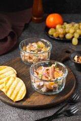 Salad of salted herring, tangerines, grapes and walnuts in portioned glass ramekins on a wooden board on a dark concrete background. Herring dishes.
