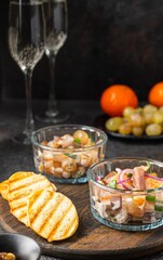 Salad of salted herring, tangerines, grapes and walnuts in portioned glass ramekins on a wooden board on a dark concrete background. Herring dishes.