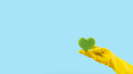 Heart shape green sponge and yellow rubber gloves on blue background. Minimal creative cleaning...