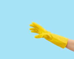 Hand in yellow rubber glove on blue background. Minimal creative cleaning service concept.