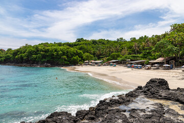 Bias Tugel beach at the south of Bali island. Many tourists swimming in blue ocean water. White sand and rock shore.
