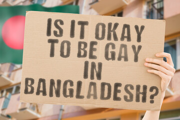 The question " Is it okay to be gay in Bangladesh? " is on a banner in men's hands with blurred background. Friendly. Passionate. Contact. Date. Dating. Lover. Partner. Boyfriend. Pleasant. Approval