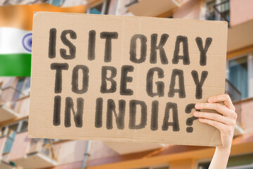 The question " Is it okay to be gay in India? " is on a banner in men's hands with blurred background. Friendly. Passionate. Contact. Date. Dating. Lover. Partner. Boyfriend. Pleasant. Approval
