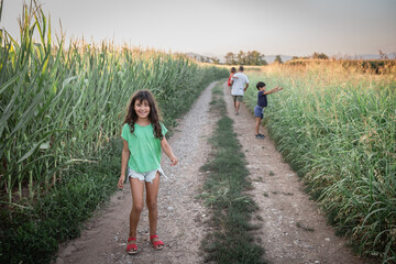 smiling girl with long hair stands on the country road with her sisters and father behind