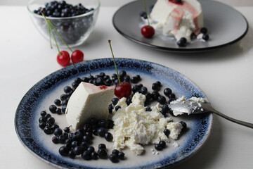 ricotta cheese with blueberries cherries on a plate close-up on a white background. Healthy food summer dessert. Cottage cheese dessert