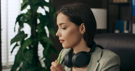 Selective focus close up shot on woman in headphones who sits at home in office work onlne from distance holds paper in hands discusses new project with coleagues .