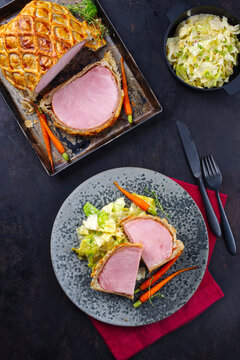 Gebackenes Kasseler Schweinesteak im Teigmantel mit Wirsing Kohl und Baby Karotten serviert als Draufsicht auf einem Nordic Design Teller und Tablett