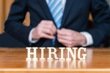 HIRING spelled out in letter tiles on desk with business person.