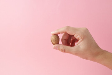 Hand holding one walnut on pink background