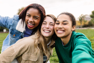 Multi-ethnic group of three young women taking a selfie having fun outdoor. Portrait of smiling diverse females enjoying time together in city park - Powered by Adobe