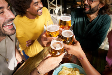 Close up of A group of colleague workers toast with beer in the restaurant bar after work at the pub happy hour. Happy friends having fun together drinking alcohol indoors.