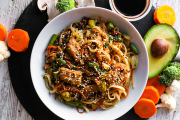 Wok, noodles, udon with chicken, on black plate and a wooden white background top view