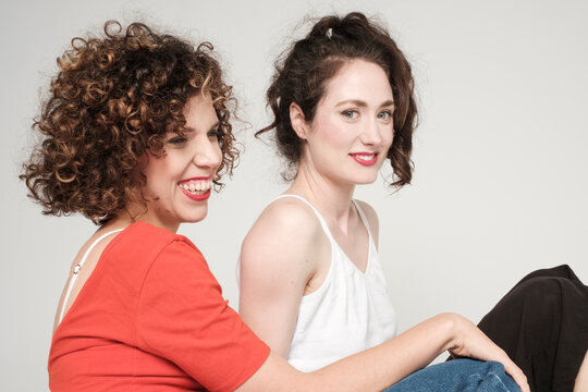 Two women friends posing on white background, smiling, happy