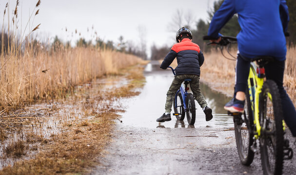 Two boys riding their bikes through a large puddle on a flooded trail.
