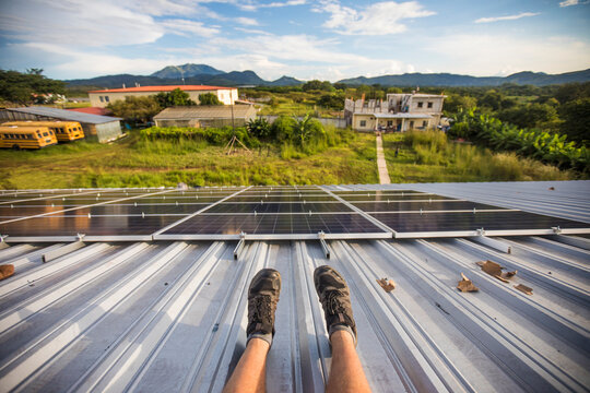 High angle view of workers legs and installed solar panels from roof.