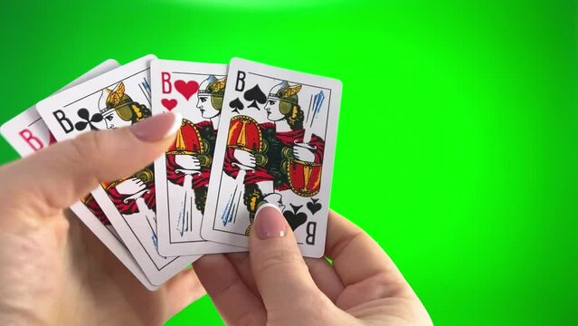 Hand holding four Jack card on a green background close-up female hands with french manicure. woman sorts through cards, examines them folds and spreads out like fan four cards left of same suit