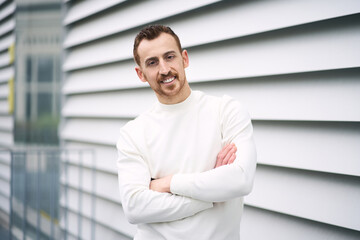 Authentic portrait of smiling attractive man with arms crossed looking at camera standing on urban street 