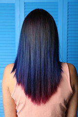 Young woman with bright dyed hair on blue wooden background, back view