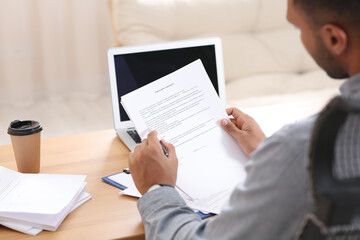 Man working with documents at wooden table in office, back view