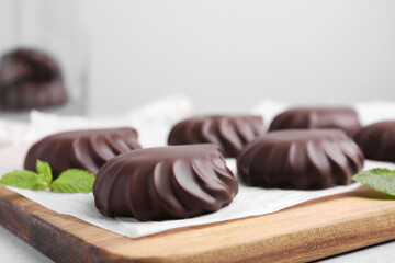 Delicious chocolate covered zephyrs and mint on wooden board, closeup