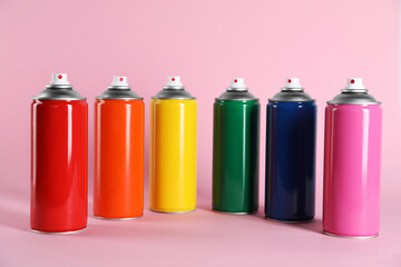 Colorful cans of spray paints on pink background