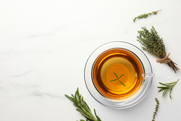 Cup of aromatic herbal tea with thyme and rosemary on white marble table, flat lay. Space for text