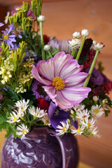 An arrangement of fresh annual and perennial garden flowers in a purple ceramic pitcher in fall