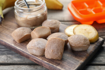 Frozen banana puree cubes and ingredient on wooden table, closeup